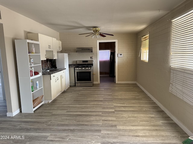 kitchen featuring white cabinetry, stainless steel range with gas cooktop, ceiling fan, and brick wall