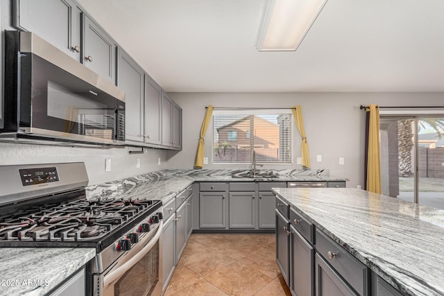 kitchen with appliances with stainless steel finishes, gray cabinetry, a sink, and light stone counters