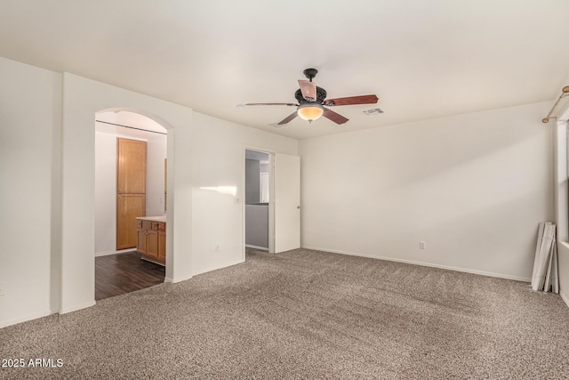 unfurnished room featuring arched walkways, visible vents, dark carpet, and a ceiling fan