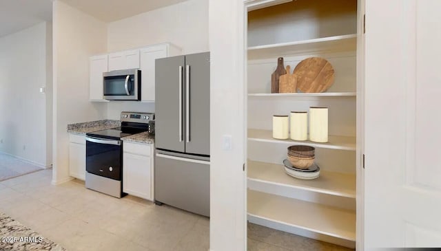 kitchen featuring light stone countertops, white cabinetry, stainless steel appliances, and light tile patterned flooring