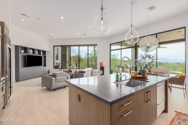 kitchen with visible vents, an island with sink, a sink, light wood-style floors, and modern cabinets