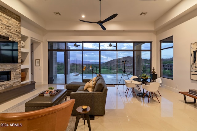 living room with a fireplace, built in shelves, ceiling fan, light tile patterned floors, and a mountain view