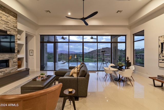 living area with baseboards, ceiling fan, light tile patterned floors, a stone fireplace, and a mountain view