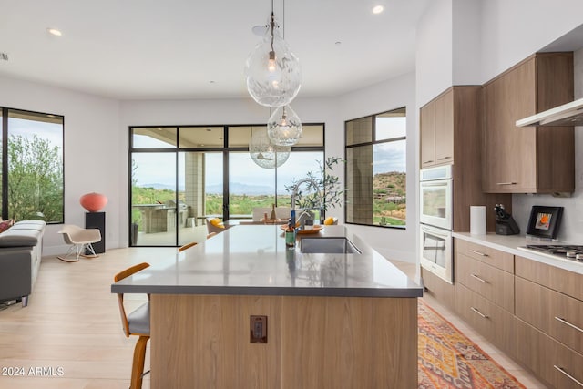 kitchen featuring stainless steel gas cooktop, modern cabinets, wall chimney range hood, and a sink