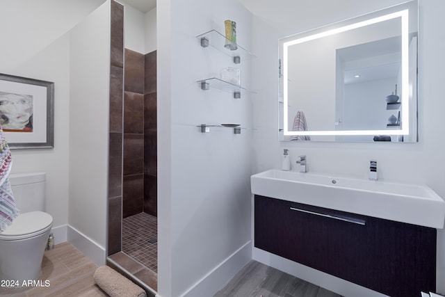 bathroom with toilet, wood finished floors, a tile shower, baseboards, and vanity