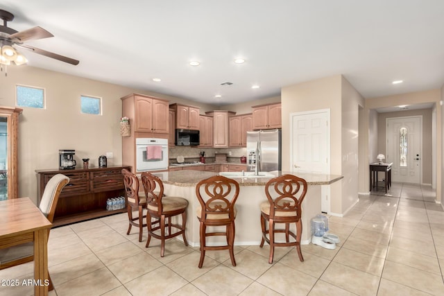kitchen with light stone counters, a sink, black microwave, stainless steel refrigerator with ice dispenser, and backsplash