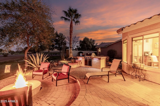 patio terrace at dusk with a fire pit, an outdoor kitchen, and area for grilling
