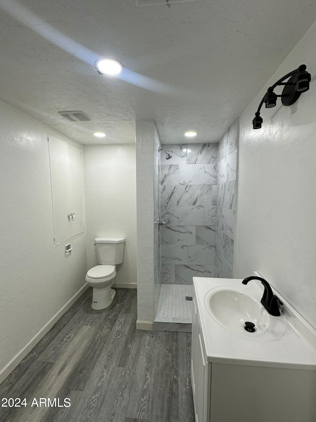 bathroom featuring vanity, hardwood / wood-style flooring, a tile shower, toilet, and a textured ceiling