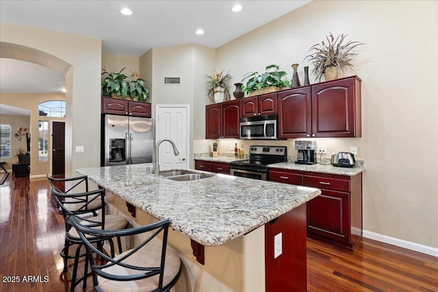 kitchen featuring a kitchen bar, dark hardwood / wood-style flooring, stainless steel appliances, sink, and a center island with sink