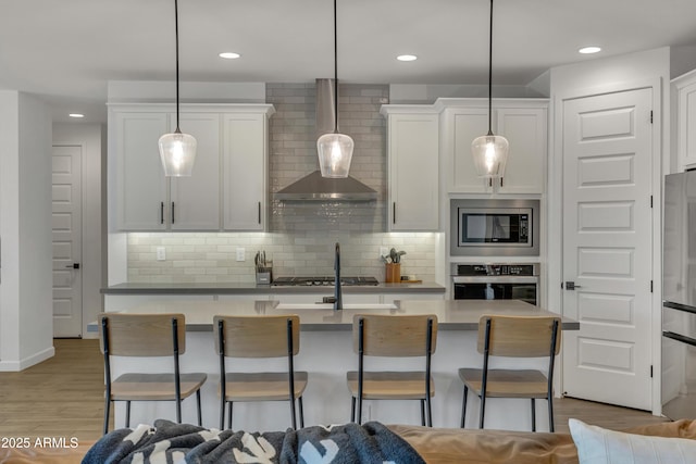 kitchen with stainless steel appliances, a breakfast bar area, white cabinets, and wall chimney exhaust hood