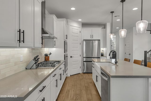 kitchen featuring light wood-style flooring, a sink, appliances with stainless steel finishes, decorative backsplash, and wall chimney exhaust hood