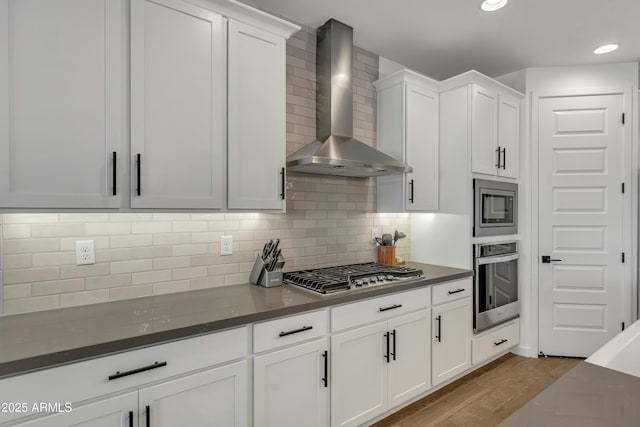 kitchen with stainless steel appliances, dark countertops, white cabinetry, wall chimney range hood, and wood finished floors