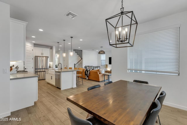 dining space with light wood finished floors, recessed lighting, visible vents, an inviting chandelier, and stairs