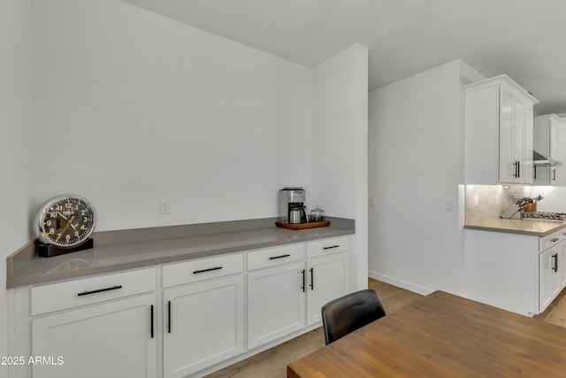 kitchen with light wood finished floors, wall chimney exhaust hood, tasteful backsplash, and white cabinets