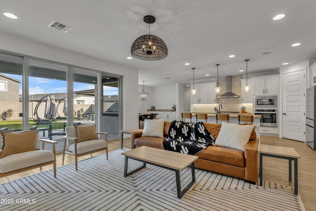 living room with recessed lighting, visible vents, light wood-style flooring, and an inviting chandelier