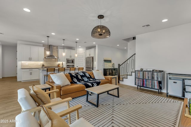 living room featuring visible vents, light wood-style flooring, an inviting chandelier, stairs, and recessed lighting