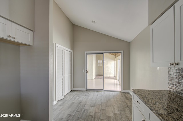 kitchen featuring white cabinetry, lofted ceiling, dark stone countertops, and light wood-type flooring