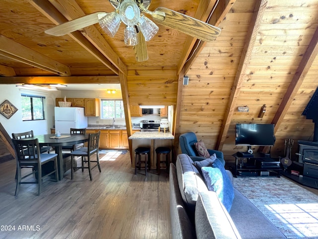 living area featuring beam ceiling, light wood finished floors, wooden ceiling, and a wood stove