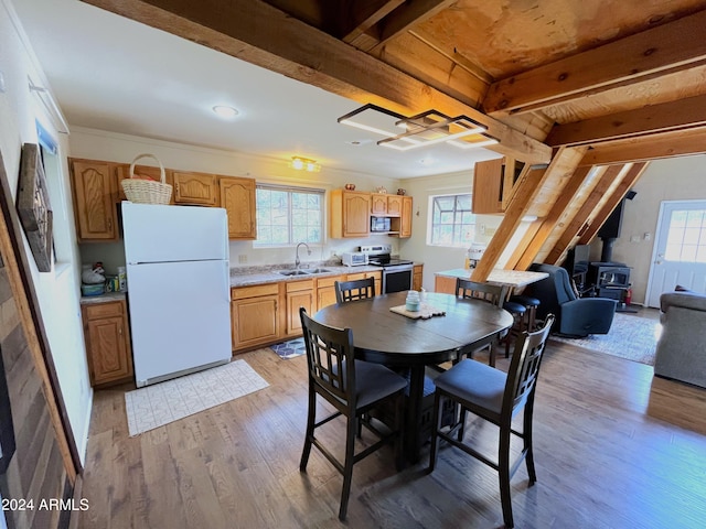 dining room with beam ceiling, a healthy amount of sunlight, a wood stove, and light wood finished floors