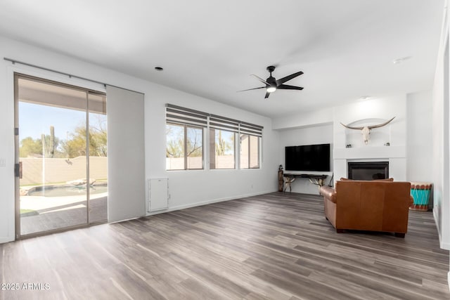 unfurnished living room featuring baseboards, a fireplace, a ceiling fan, and wood finished floors