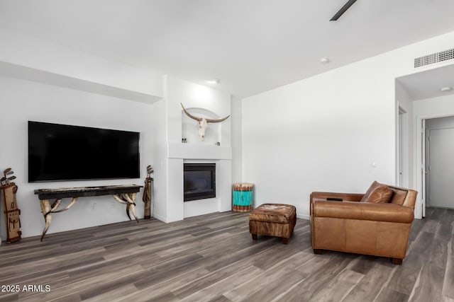 living area with a glass covered fireplace, visible vents, and wood finished floors