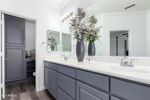 full bath featuring wood finished floors, a sink, visible vents, double vanity, and crown molding