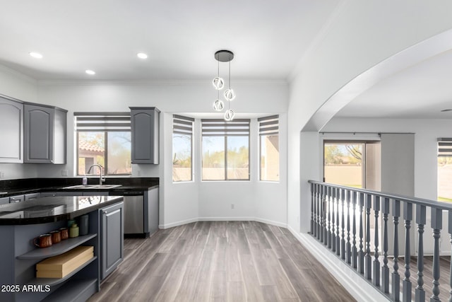 kitchen featuring arched walkways, dark countertops, wood finished floors, gray cabinetry, and a sink