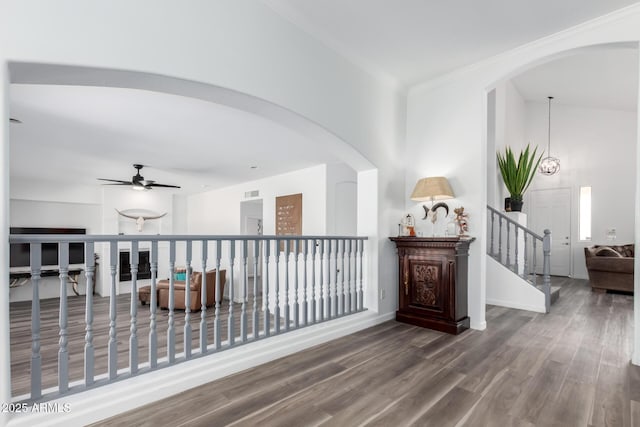 hallway featuring arched walkways, wood finished floors, baseboards, ornamental molding, and stairway