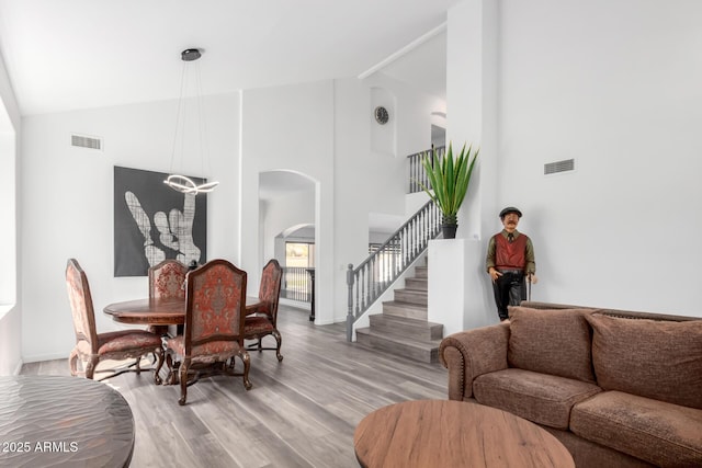 living area featuring arched walkways, stairway, light wood-type flooring, and visible vents