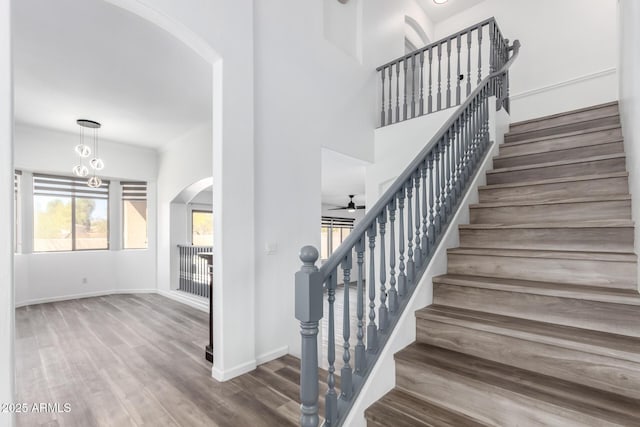 stairway featuring ceiling fan, arched walkways, wood finished floors, a towering ceiling, and baseboards