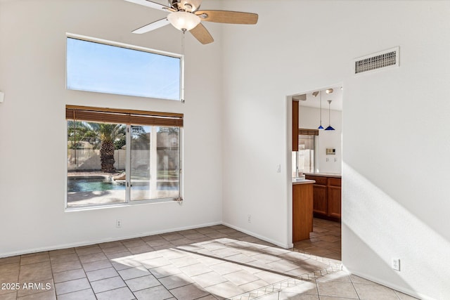 empty room featuring ceiling fan, light tile patterned floors, and a high ceiling