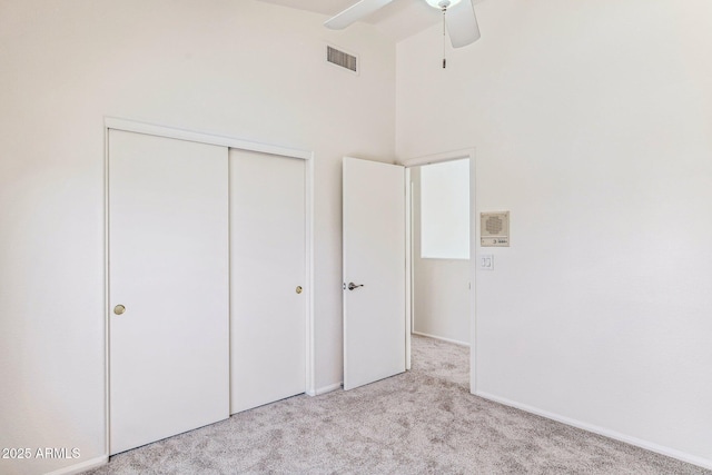 unfurnished bedroom with ceiling fan, a high ceiling, a closet, and light carpet