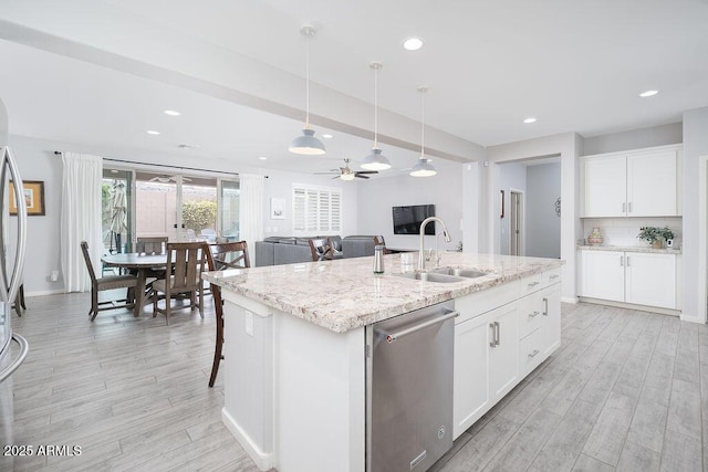 kitchen with a sink, light wood-style floors, appliances with stainless steel finishes, tasteful backsplash, and a center island with sink