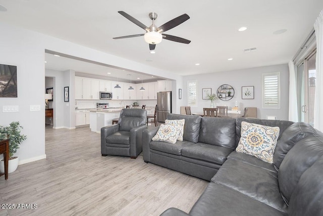 living room with baseboards, visible vents, a ceiling fan, light wood-style floors, and recessed lighting