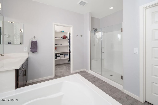 full bath with wood finished floors, vanity, visible vents, a stall shower, and a walk in closet