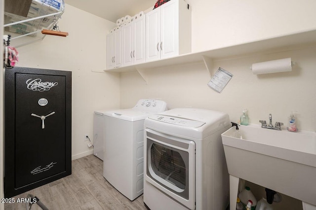 laundry area featuring a sink, baseboards, cabinet space, light wood finished floors, and washing machine and clothes dryer