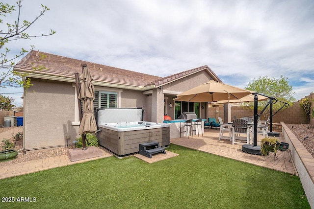 back of property with a patio, stucco siding, a lawn, a hot tub, and a fenced backyard