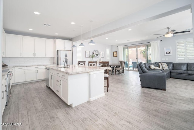 kitchen featuring light wood finished floors, visible vents, a sink, stainless steel appliances, and backsplash