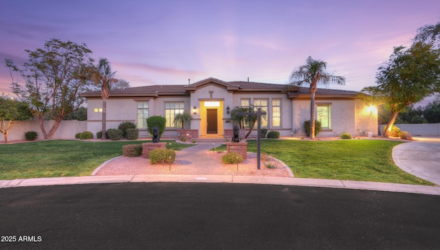 view of front of home featuring fence, a lawn, and stucco siding