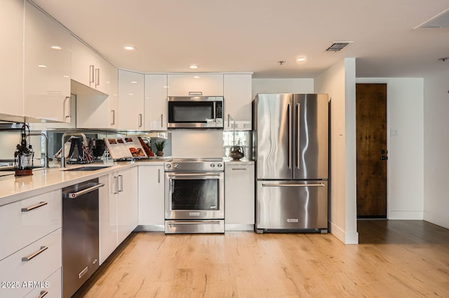 kitchen with high quality appliances, sink, light hardwood / wood-style flooring, and white cabinets