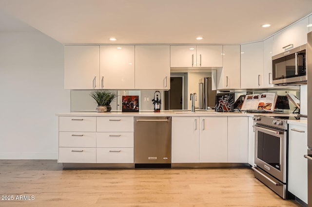 kitchen with white cabinetry, appliances with stainless steel finishes, sink, and light hardwood / wood-style flooring