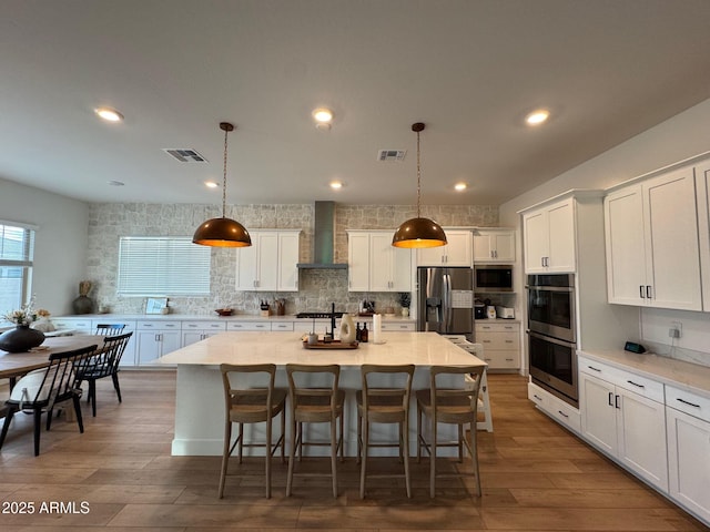 kitchen featuring backsplash, appliances with stainless steel finishes, white cabinets, wall chimney range hood, and wood finished floors