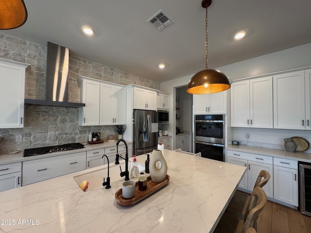 kitchen featuring visible vents, white cabinets, hanging light fixtures, stainless steel appliances, and wall chimney range hood