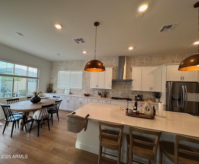 kitchen with backsplash, visible vents, stainless steel refrigerator with ice dispenser, and wall chimney exhaust hood