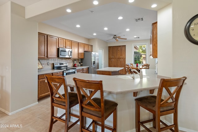 kitchen featuring a kitchen breakfast bar, sink, ceiling fan, light tile patterned floors, and appliances with stainless steel finishes