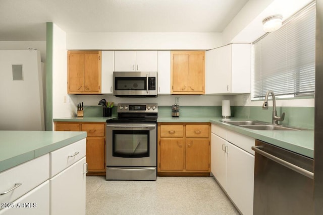 kitchen featuring appliances with stainless steel finishes, a sink, light countertops, and white cabinetry