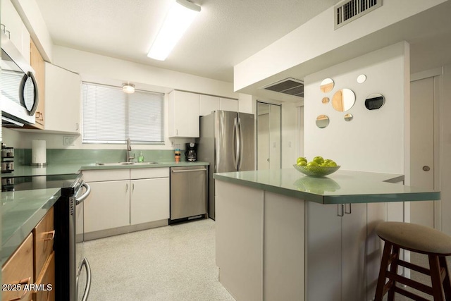 kitchen with appliances with stainless steel finishes, a sink, a breakfast bar area, and white cabinetry