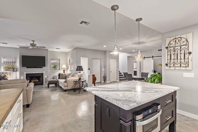 kitchen with ceiling fan, stainless steel oven, a barn door, pendant lighting, and white cabinets