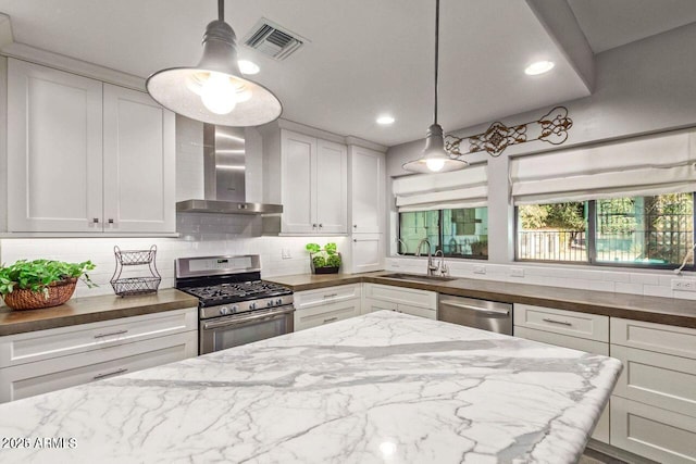 kitchen with pendant lighting, white cabinets, sink, wall chimney exhaust hood, and appliances with stainless steel finishes