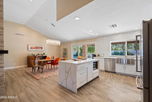 kitchen with appliances with stainless steel finishes, hanging light fixtures, vaulted ceiling, white cabinets, and light hardwood / wood-style flooring